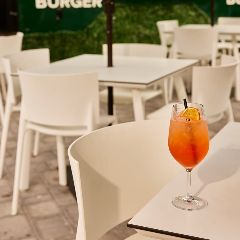 Orange cocktail with an orange slice and straw on a white table at PROPER BURGER Downtown.