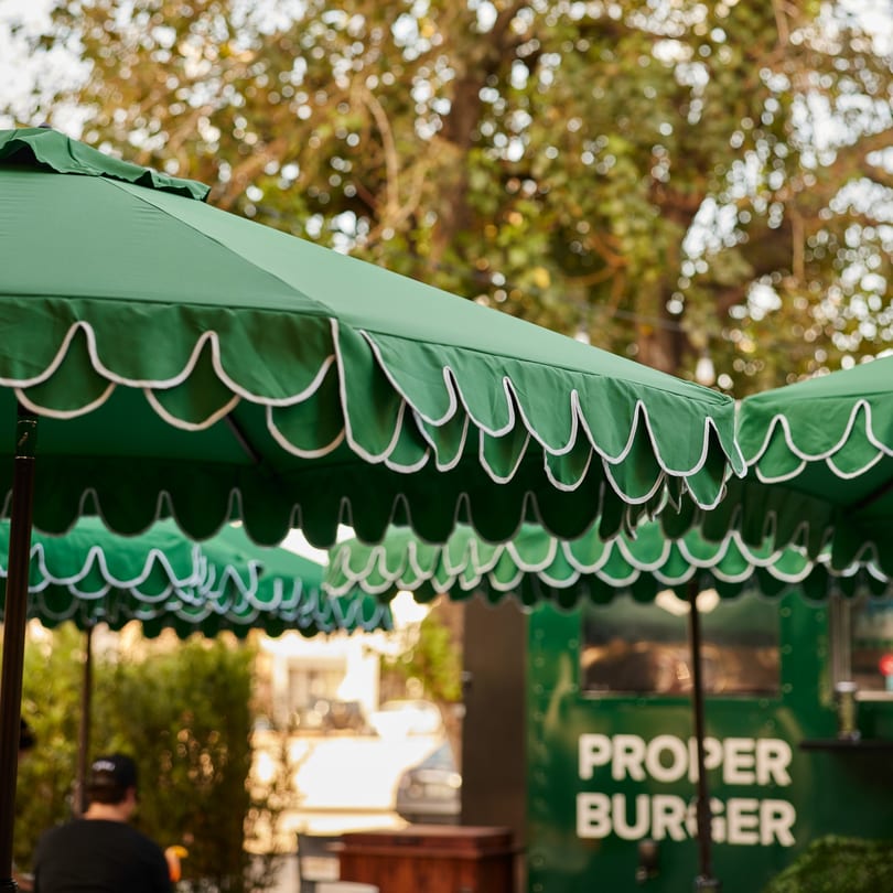 Green scalloped umbrellas provide shade over outdoor seating at PROPER BURGER Downtown.