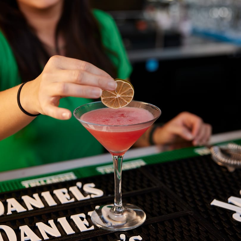 A bartender garnishes a pink martini with a dried citrus slice at PROPER BURGER Downtown.