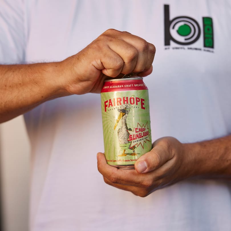 Hands opening a can of Fairhope Brewing Company's "Cheap Sunglasses" Golden Ale.