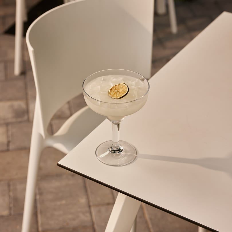 A Proper Burger Downtown cocktail with a dried lime slice sits on a white outdoor table.