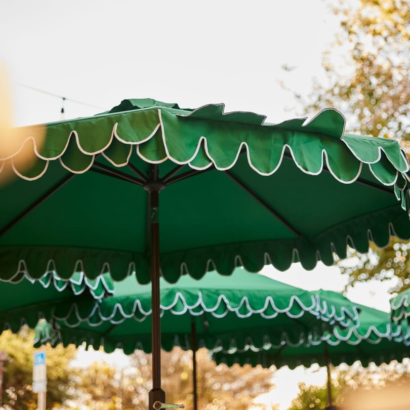 Green scalloped patio umbrellas with white trim provide shade for outdoor dining at PROPER BURGER Downtown.