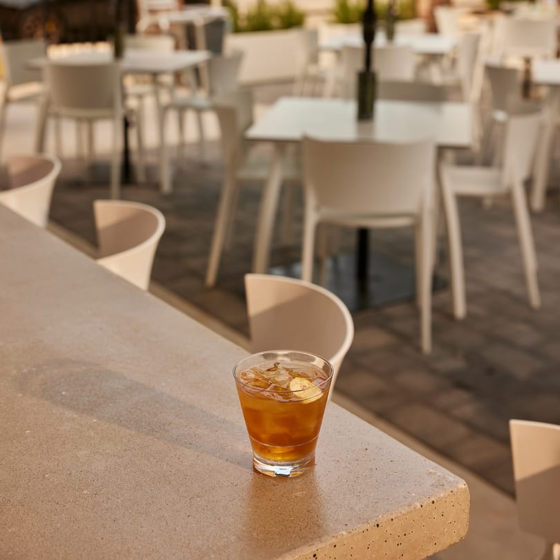 An iced drink with a lemon slice on a bar, with an outdoor patio in the background.