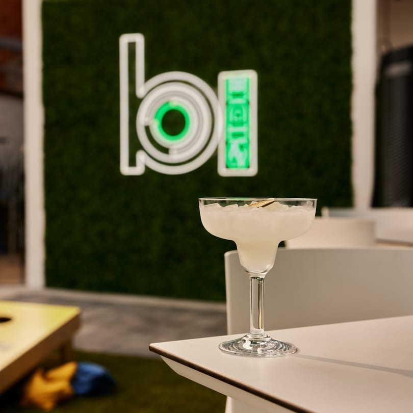 A margarita on a white table with a green neon "Proper Burger" sign in the background.