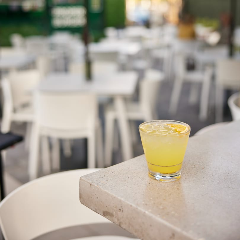 A yellow drink with ice and a lemon slice sits on a concrete bar at PROPER BURGER Downtown.