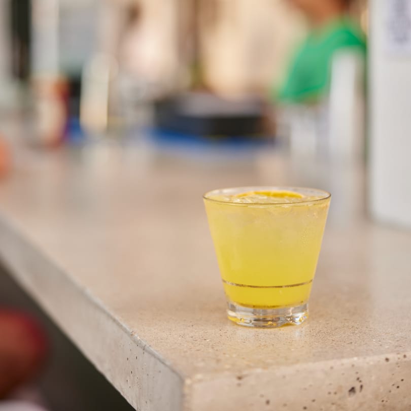 A refreshing yellow drink with ice and a lemon slice sits on a light-colored counter.