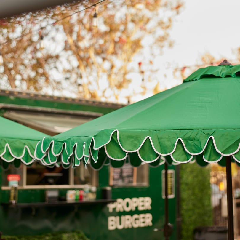 Green umbrellas with white scalloped edges partially obscure the Proper Burger food truck.